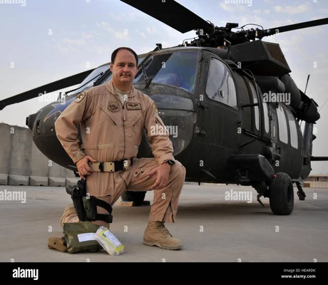 Militaire en tenue de vol devant un Black Hawk lors d'une évacuation médicale à Bagdad, avec du matériel au sol sur un aérodrome.