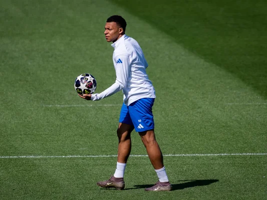 Kylian Mbappé en maillot blanc les bras ouverts sur le terrain.