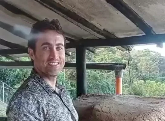 Julien Février debout sous un béton armé entouré de verdure, portant une chemise à motif.