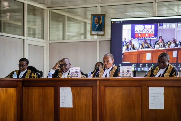 Quatre juges en robe dans une salle d'audience, devant un écran de visioconférence.