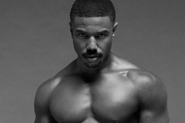 Michael B. Jordan en noir et blanc, mettant en valeur sa musculature sur fond uni.