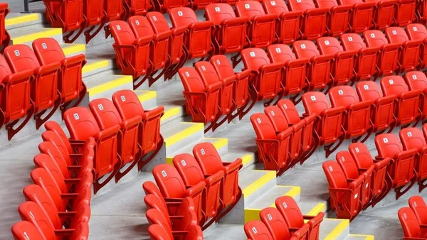 Des sièges de stade rouges numérotés vides, disposés en gradins avec des marches jaunes.