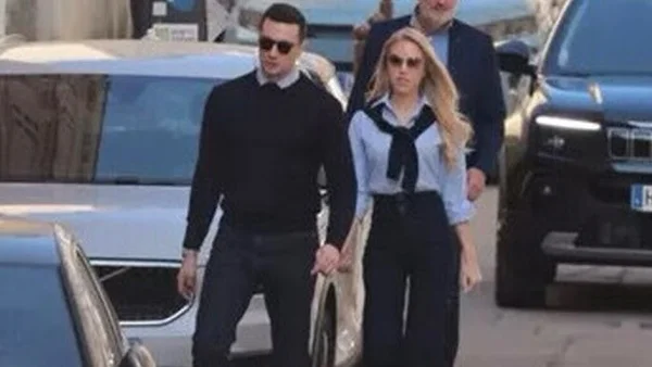 Jordan Bardella et sa compagne se promènent main dans la main dans une rue, entourés de véhicules.