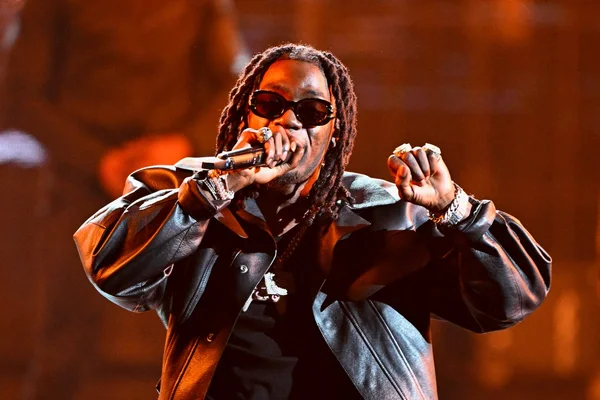 Le rappeur Gazo en plein concert, portant une veste en cuir et des lunettes de soleil.