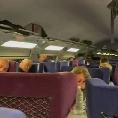 Intérieur de train montrant des passagers assis dans des sièges bleus et bordeaux.