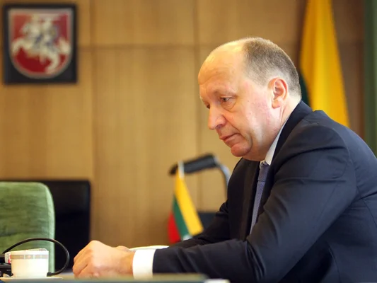 Un officiel assis lors d'une réunion, avec des drapeaux lituaniens en arrière-plan.