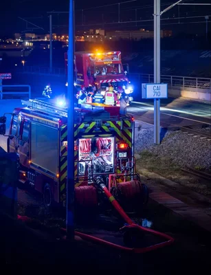 Des secouristes et un camion de pompiers intervenant près des voies ferrées la nuit.