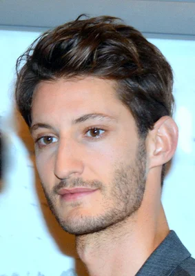 Portrait en gros plan de Pierre Niney en chemise grise.