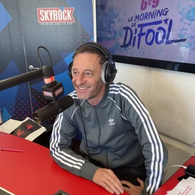 Emeric Berco à l'antenne de Skyrock, portant un casque et une chemise à rayures.