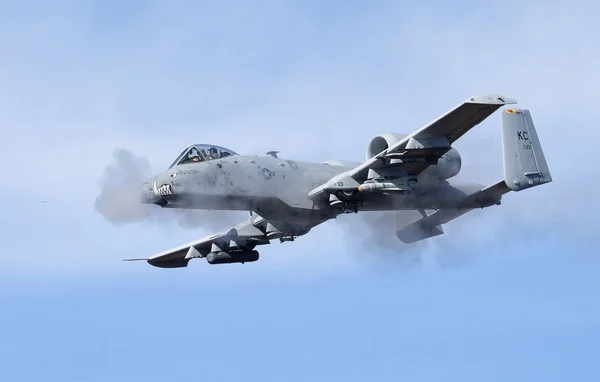 Un A-10 Thunderbolt II de l'US Air Force avec nez en bouche de requin en vol émettant de la fumée.