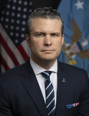 Portrait officiel de Pete Hegseth en costume sombre, devant le drapeau américain et un drapeau à l'aigle.