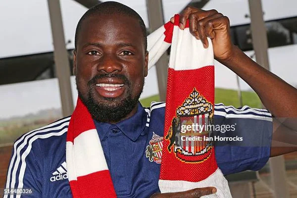 Emmanuel Eboué posant avec une écharpe de supporter et un polo Adidas bleu.