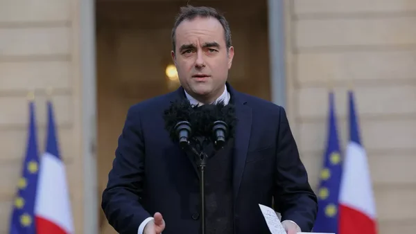 Sébastien Lecornu s'adresse à la presse depuis une tribune officielle, entouré des drapeaux français et européens.