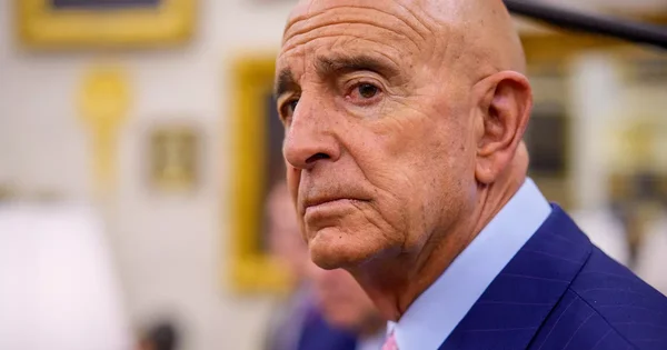 Portrait rapproché d'un homme en costume bleu sur un décor flou.