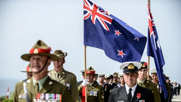 Des militaires et des officiers de marine défilant avec des drapeaux néo-zélandais.