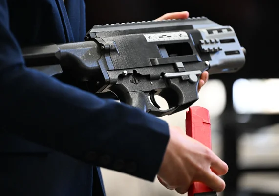 Une personne en costume tenant une arme à feu noire avec chargeur rouge, illustrant le fonctionnement des armes fantômes.