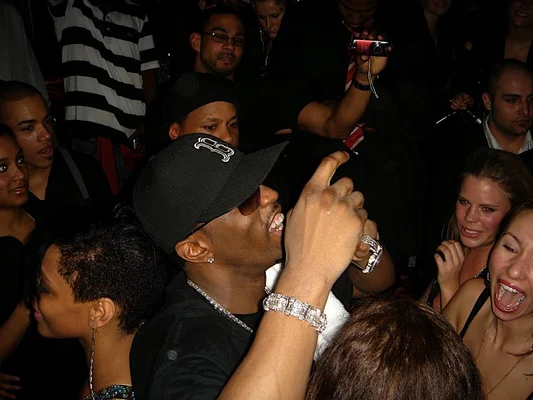 Sean Combs en 2008, coiffé d'une casquette et portant des bijoux, au centre d'une foule avec des caméras.
