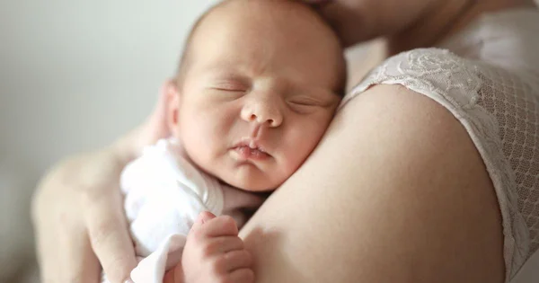 Un bébé dort contre l'épaule d'un adulte.