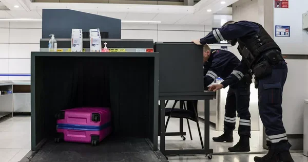 Agents de sécurité au poste de contrôle bagages de l'aéroport de Nantes, avec un scanner à rayons X et une valise rose sur le tapis