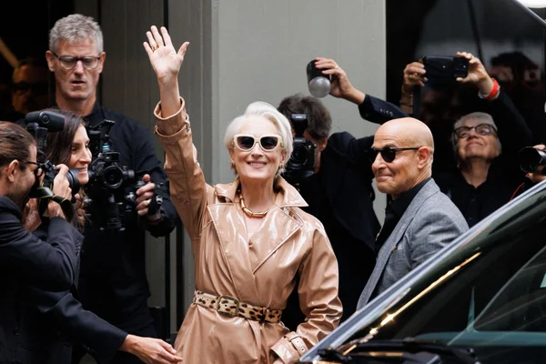 Meryl Streep en trench-coat beige saluant les photographes accompagnée d'un homme en costume gris.