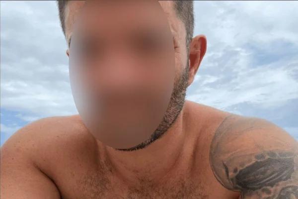Cédric Prizzon, ancien policier recherché, torse nu avec un tatouage sur le bras, photographié devant un ciel nuageux.
