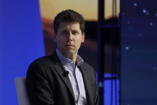 Sam Altman, PDG d'OpenAI, lors d'une apparition publique avec micro cravate devant un fond dégradé bleu.
