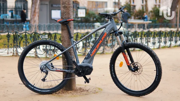 VTT électrique Nakamura E-Summit gris et orange stationné dans un parc extérieur.