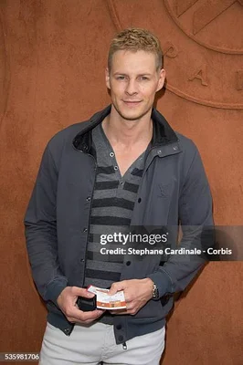 Matthieu Delormeau posant devant un mur marron en tenue décontractée grise et blanche.