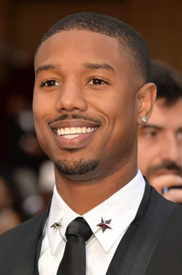 Michael B. Jordan en tenue formelle avec des bijoux remarquables, posant pour une photographie officielle.