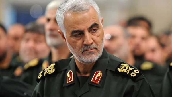 Qassem Soleimani en tenue militaire avec des insignes, entouré d'autres personnes en uniforme.