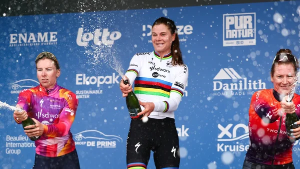 Podium de cyclistes célébrant, avec la championne du monde en maillot arc-en-ciel au centre.