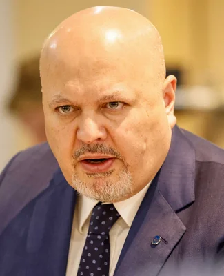 Karim Khan en veste bleue et cravate sombre, s'exprimant lors d'un événement