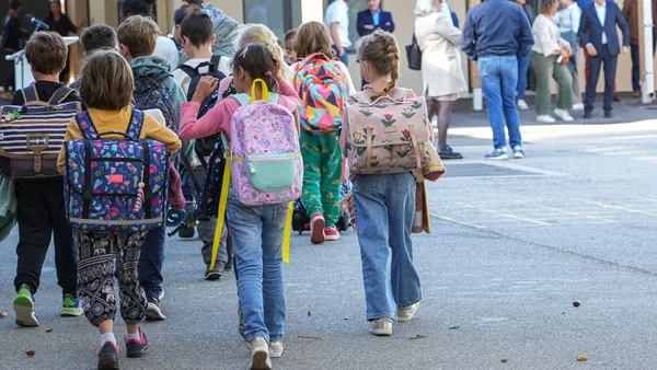 Des enfants avec des cartables colorés marchant en direction de l'école.