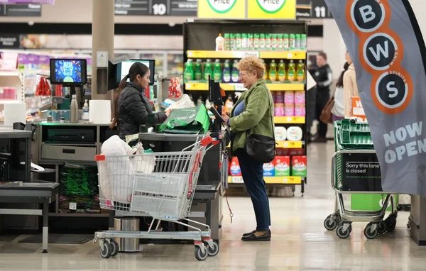 Une cliente discutant avec un caissier à une borne de paiement dans un supermarché.