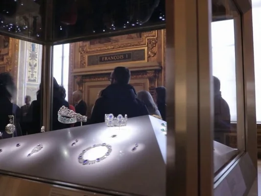 Vitrine contenant des bijoux ornés dans la salle François Ier du Louvre, observée par des visiteurs.