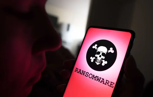 Main tenant un smartphone affichant une alerte de rançonlogiciel sur fond rouge.