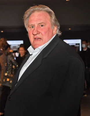 Gérard Depardieu capturé dans une expression animée, vêtu d'une chemise bleu clair.