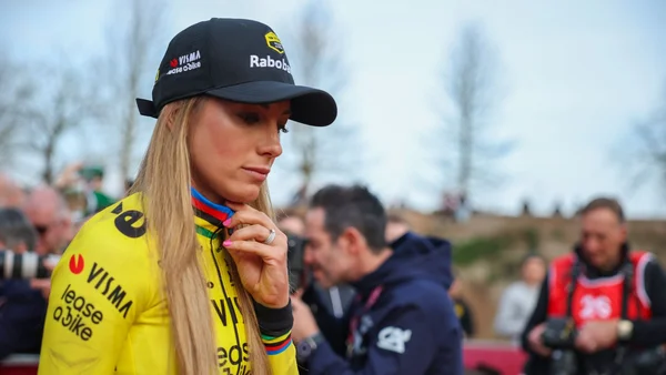 Une cycliste célèbre en levant son vélo après une course sur une route bordée de barrières et de publicités.