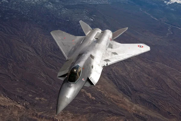 Un avion de chasse gris survolant un paysage de montagnes escarpées sous un ciel bleu.