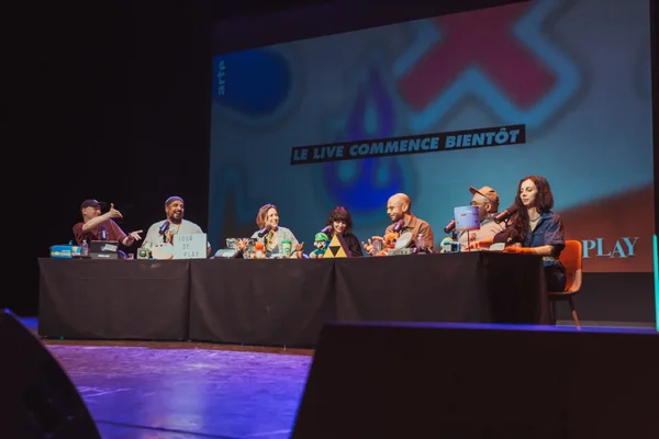Table ronde sur scène au Frames Festival avec sept intervenants devant un écran annonçant le début d'un direct