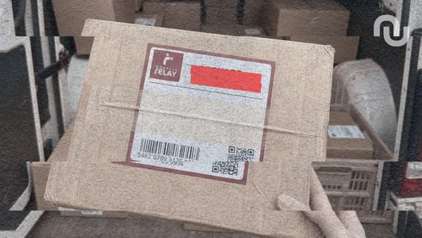 Un colis en carton muni d'une étiquette 'RELAY' et d'un code QR tenu par une main à l'intérieur d'un véhicule de livraison.