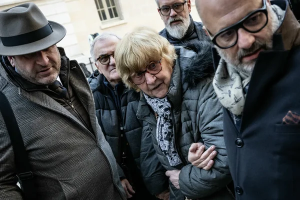 Une femme en doudoune grise soutenue par un groupe de personnes à l'extérieur.