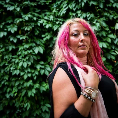 Loana avec des mèches roses dans les cheveux, devant une végétation luxuriante.