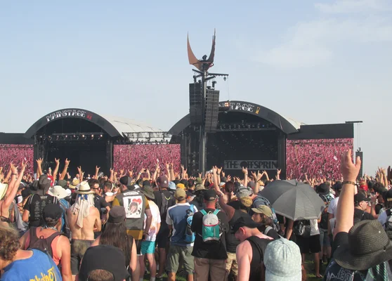 Le public du Hellfest devant des décors industriels, dont une croix rouillée et un bâtiment marqué 'war'.