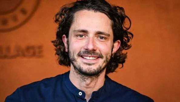 Guillaume Pley en chemise bleue souriant devant un fond orange.