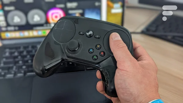 Une manette de jeu noire tenue en main devant un setup informatique, illustrant les fonctionnalités inédites attendues pour le Steam Controller 2.