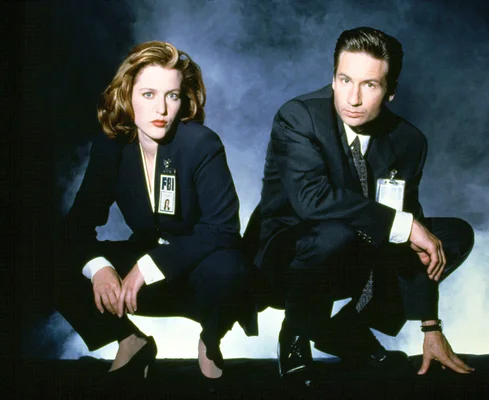 Les agents fédéraux Mulder et Scully dans une posture d'intense investigation sur fond bleu.