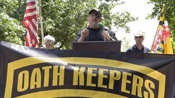 Le leader des Oath Keepers Stewart Rhodes parlant à un micro devant une bannière de son groupe.