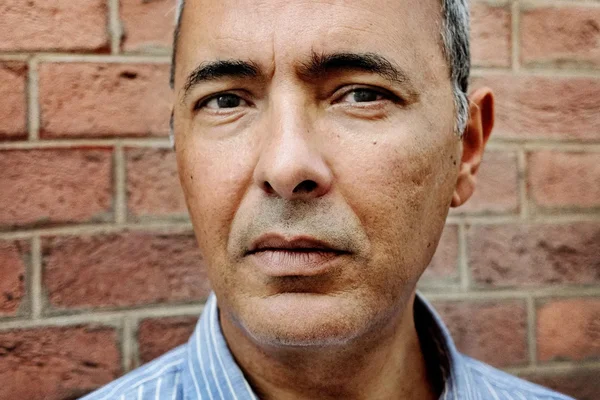 Kamel Daoud posant devant un mur de briques rouges.