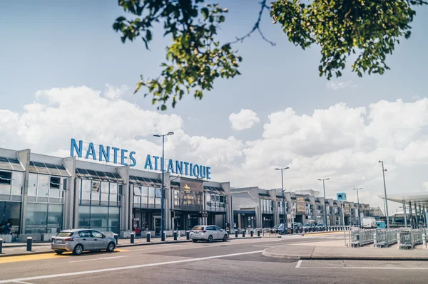 La façade de l'aéroport Nantes Atlantique avec son nom affiché en bleu et des véhicules à proximité.